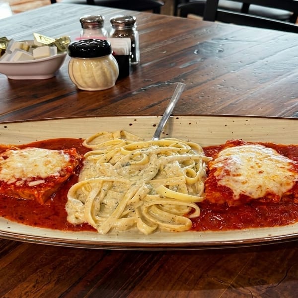 Chicken parmesan with fettuccine alfredo on a rectangular plate at a rustic wooden table.