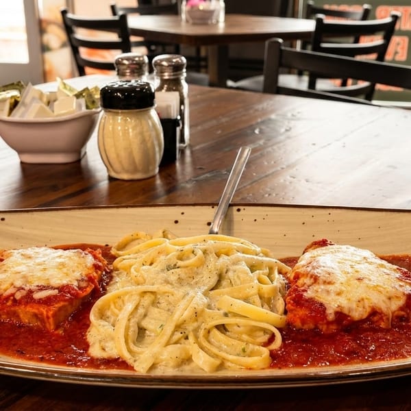 Chicken parmesan with fettuccine alfredo on a rustic wooden table in a restaurant setting.