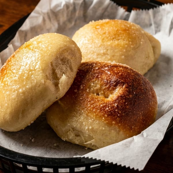 Three golden-brown bread rolls with a sprinkle of salt, served in a basket lined with parchment paper.